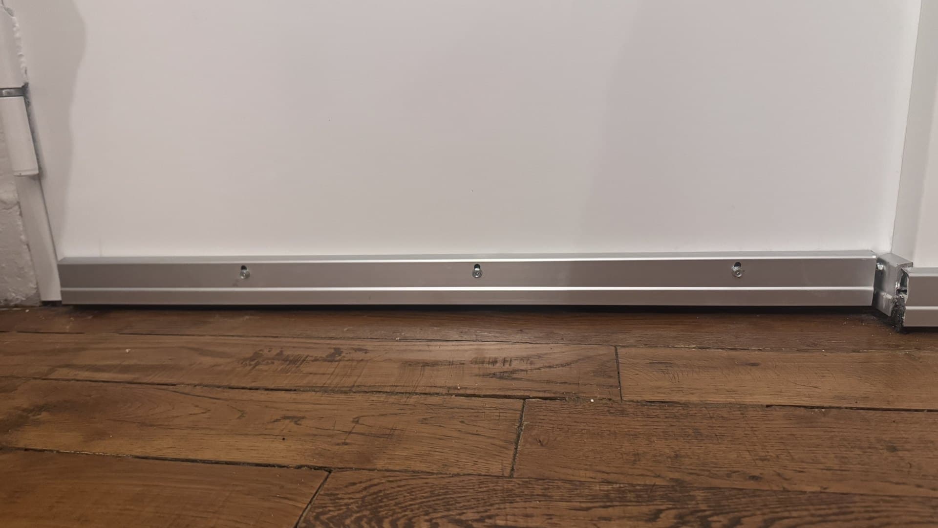 Bas de porte aluminium anti-rongeurs posé sur un parquet parisien